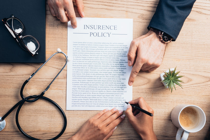 top view of lawyer pointing with finger at insurance policy agreement near client, cup of coffee stethoscope and plant